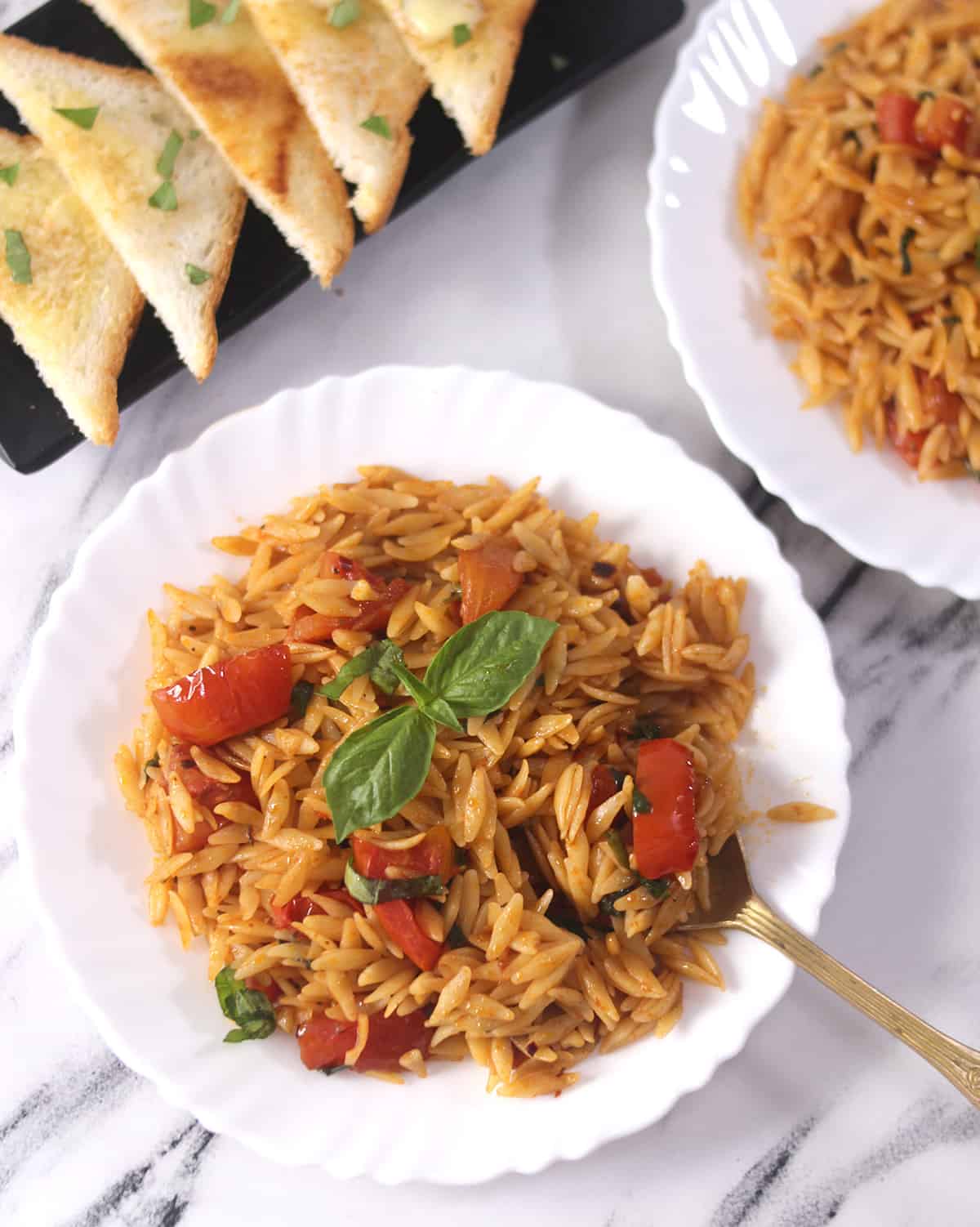 Orzo pasta on a white serving plate with golden spoon and toasted bread slices. 