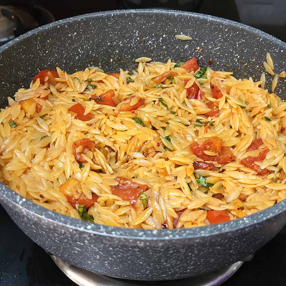 Warm orzo pasta with tomatoes and basil in pan.