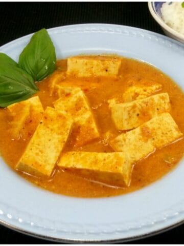 Easy homemade Pad Ped Tofu in a white bowl garnished with Basil leaves.