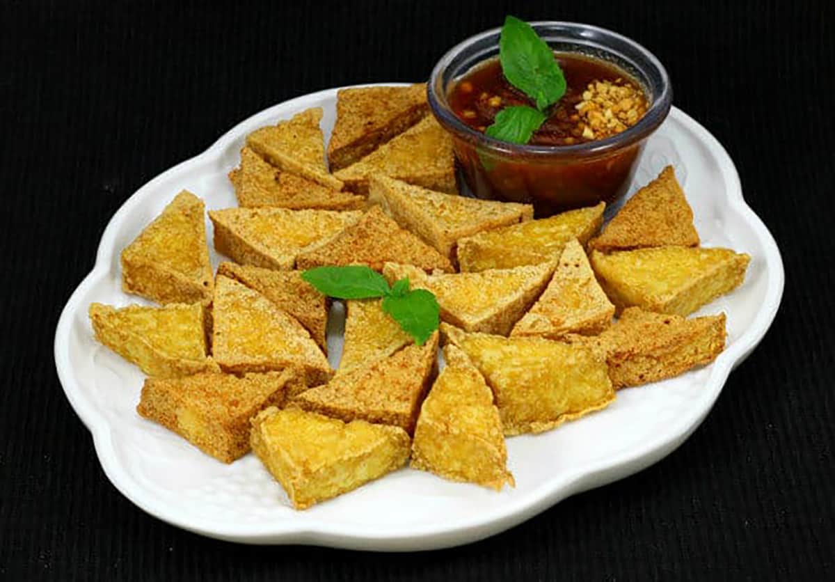 Crispy fried tofu with Thai peanut dipping sauce on white serving plate. 