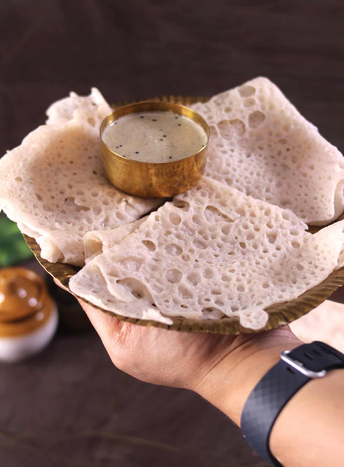 holding plate of perfectly made neer dosa with chutney, lacy thin and soft indian crepes, rice dosa