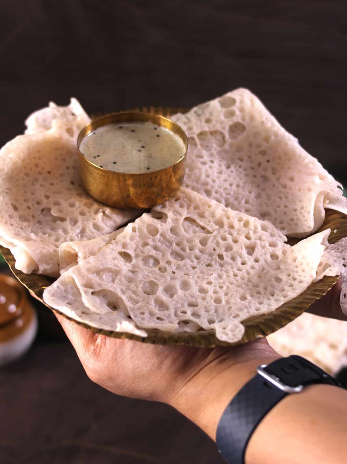 holding bronze plate with 3 neer dosa, neeru dose or pan polo, traditional Mangalorean recipe 