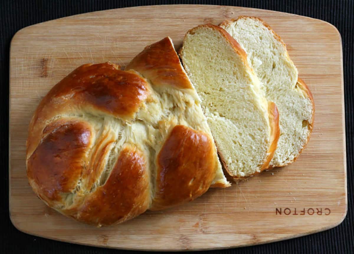 Braided challah bread loaf with 2 slices on a serving board. 