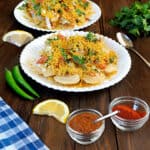 Street style sev puri on a white plate with papdi chaat in the background.