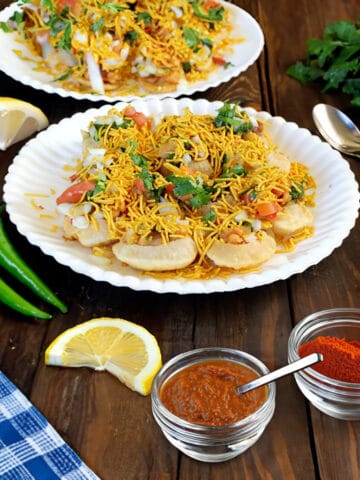 Street style sev puri on a white plate with papdi chaat in the background.