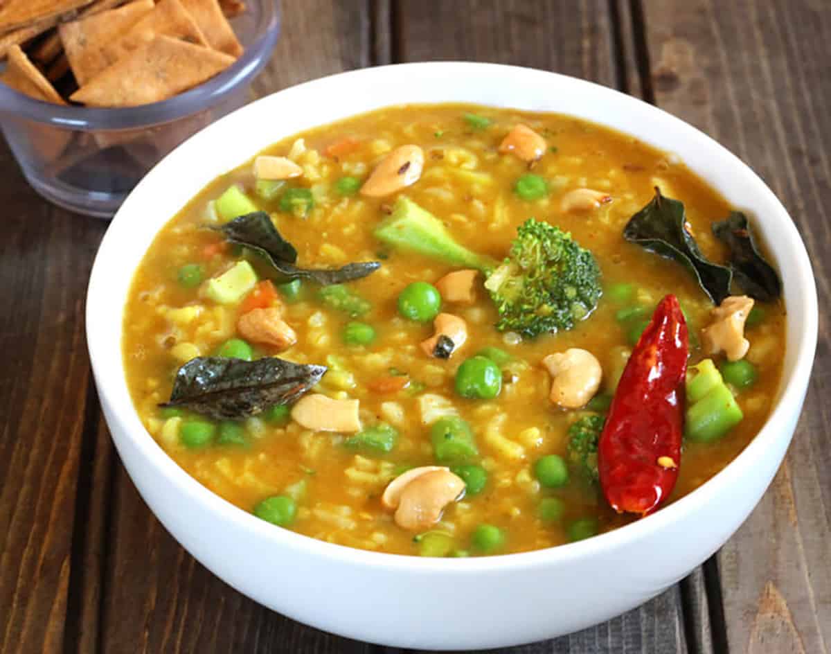 Spicy bisi bele bhaat or lentil rice in a white serving bowl garnished with cashews, curry leaves