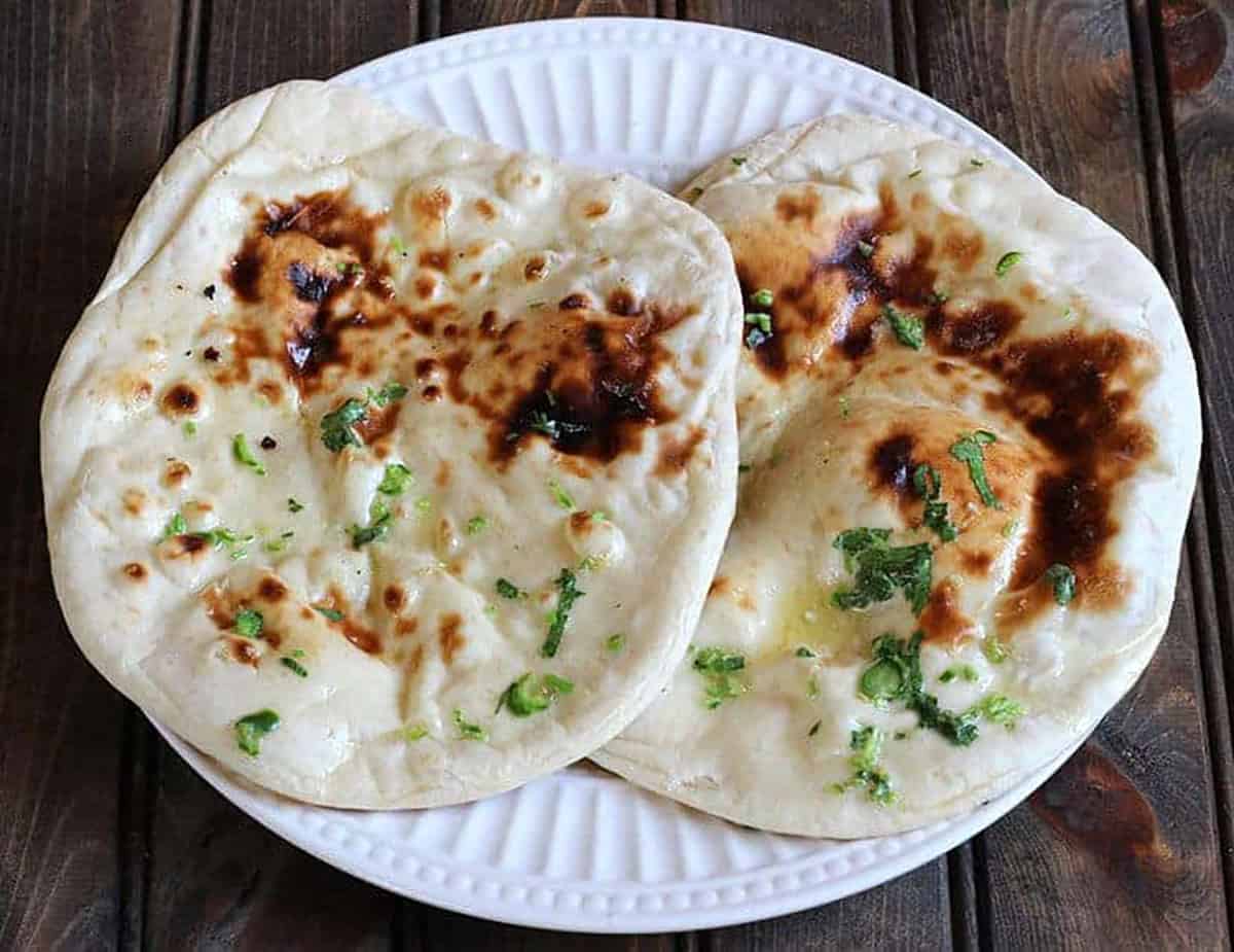 tawa naan served on white plate brushed with butter, herbs. 