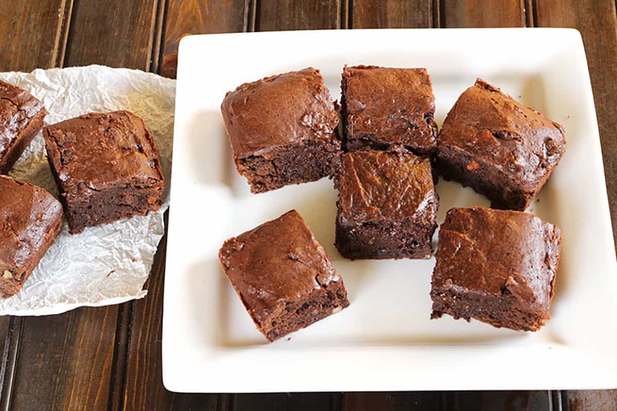 Thick chocolate brownie slices on white plate and parchment paper. 