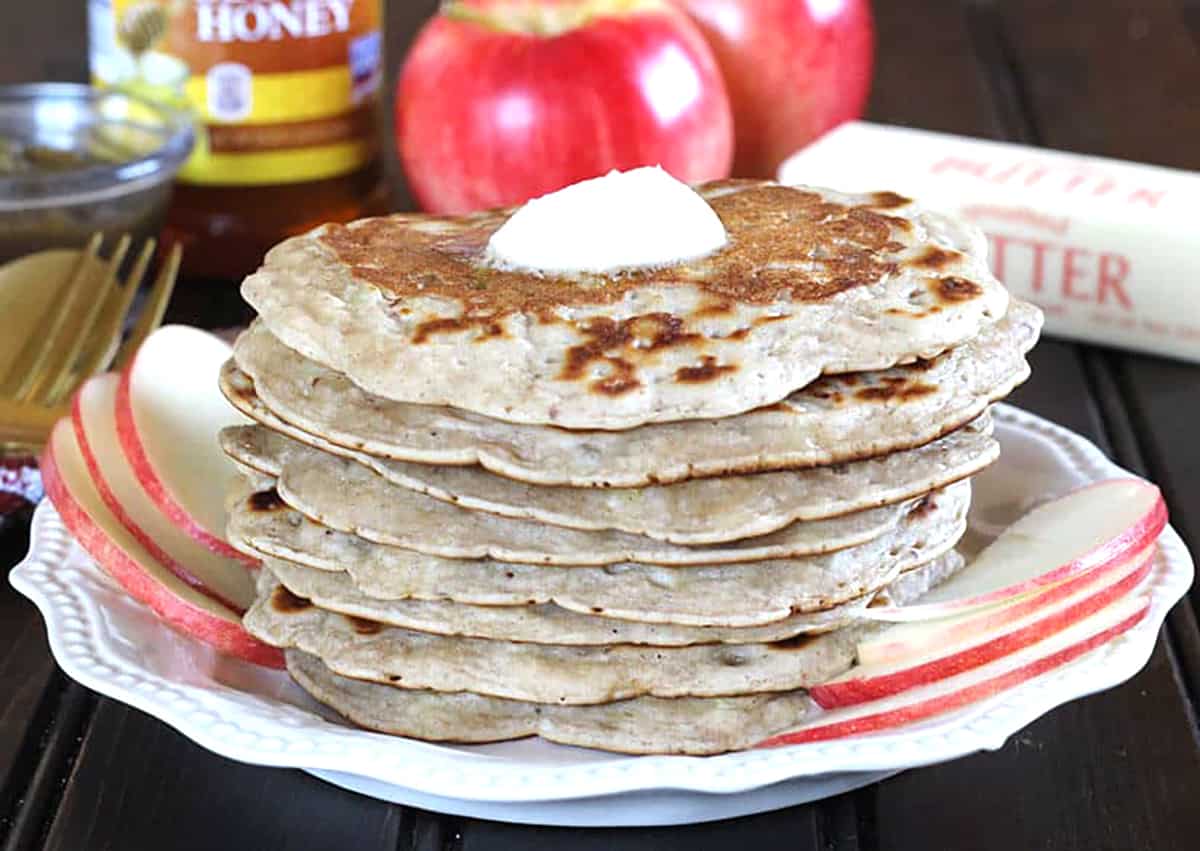 Stack of homemade vegan apple pancakes with apple butter, flour, cinnamon, milk, sugar, oil, nutmeg.