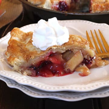 Slice of easy flaky homemade apple blackberry pie in a serving plate topped with whipped cream.