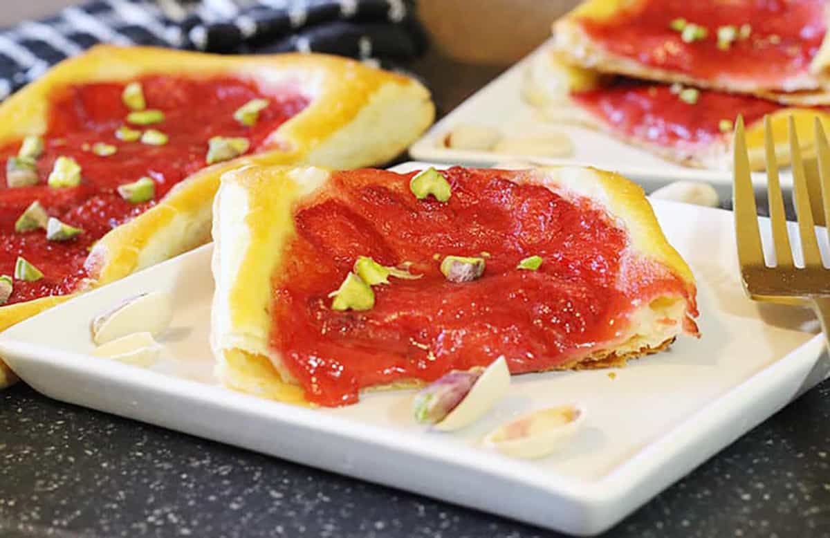 Easy strawberry tarts with puff pastry garnished with pistachios on a white plate. 