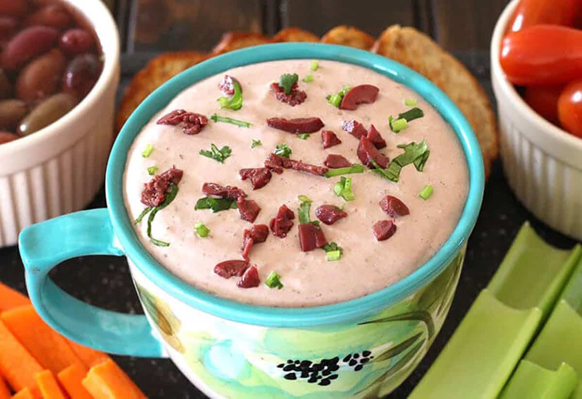 Cream cheese olive dip (spread) in a bowl, garnished with olives and fresh herbs. 