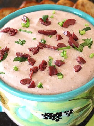 Cream cheese olive dip (spread) garnished with chopped kalamata olives and fresh herbs.