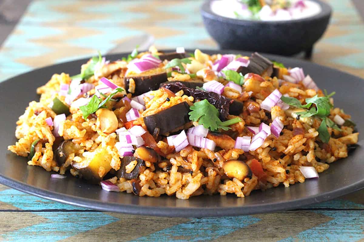 delicious aubergine or eggplant rice on a black plate garnished with onions.