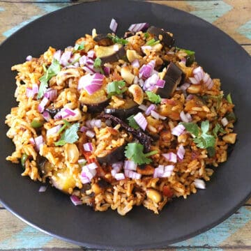 Best eggplant rice or vangi bath served on black plate garnished with onion and coriander leaves.