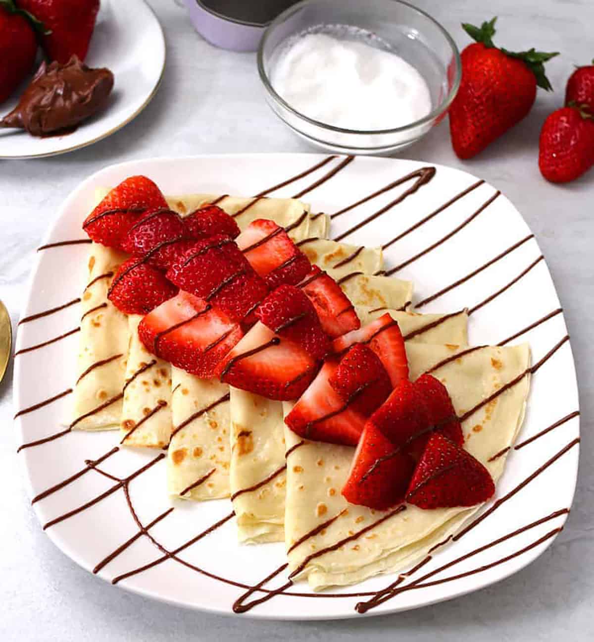 Nutella Crepes topped with strawberries on a white serving plate. 