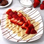 Easy Nutella Crepes topped with fresh strawberries on white serving plate.