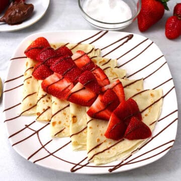 Easy Nutella Crepes topped with fresh strawberries on white serving plate.