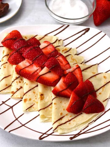 Easy Nutella Crepes topped with fresh strawberries on white serving plate.