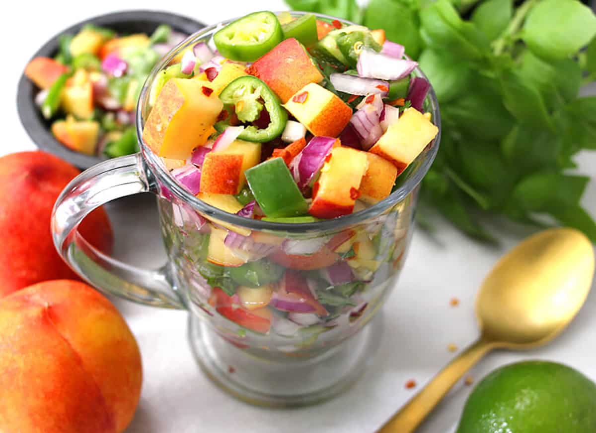 Summer salsa made with peaches, cilantro, jalapeno, lime in a glass bowl. 
