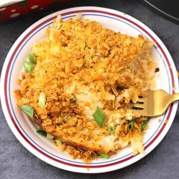 cheesy potato casserole served in a white plate with golden fork.