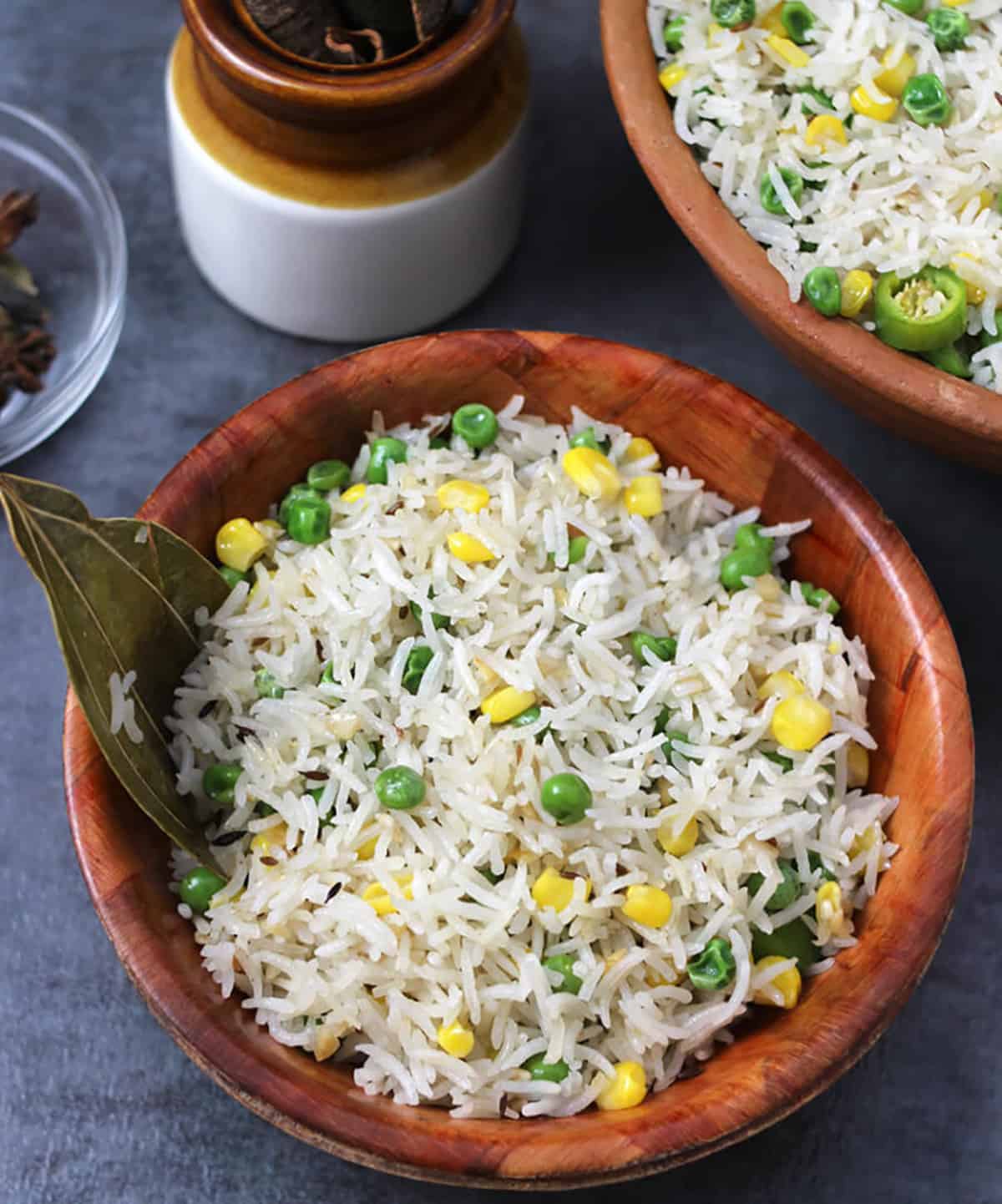 Temple style ghee rice served on brown bowl with bay leaf, corn, green peas