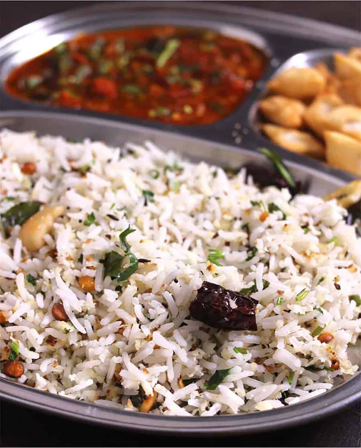 Indian coconut rice (thengai sadam or kobbari annam) served in a plate with curry and fryums. 