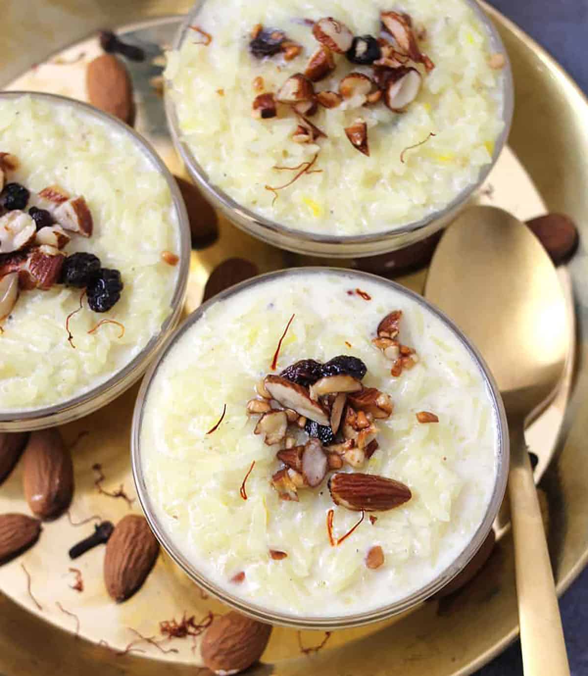 Indian rice kheer served in 3 glass bowls and golden brass plate garnished with dry fruits and nuts 