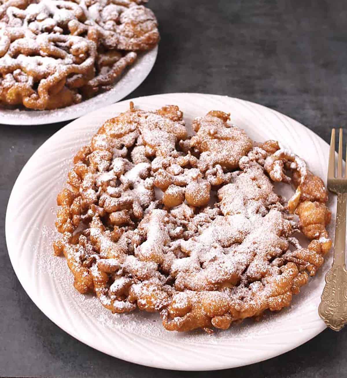 Big crispy funnel cake served on a plate that is topped with confectioners sugar