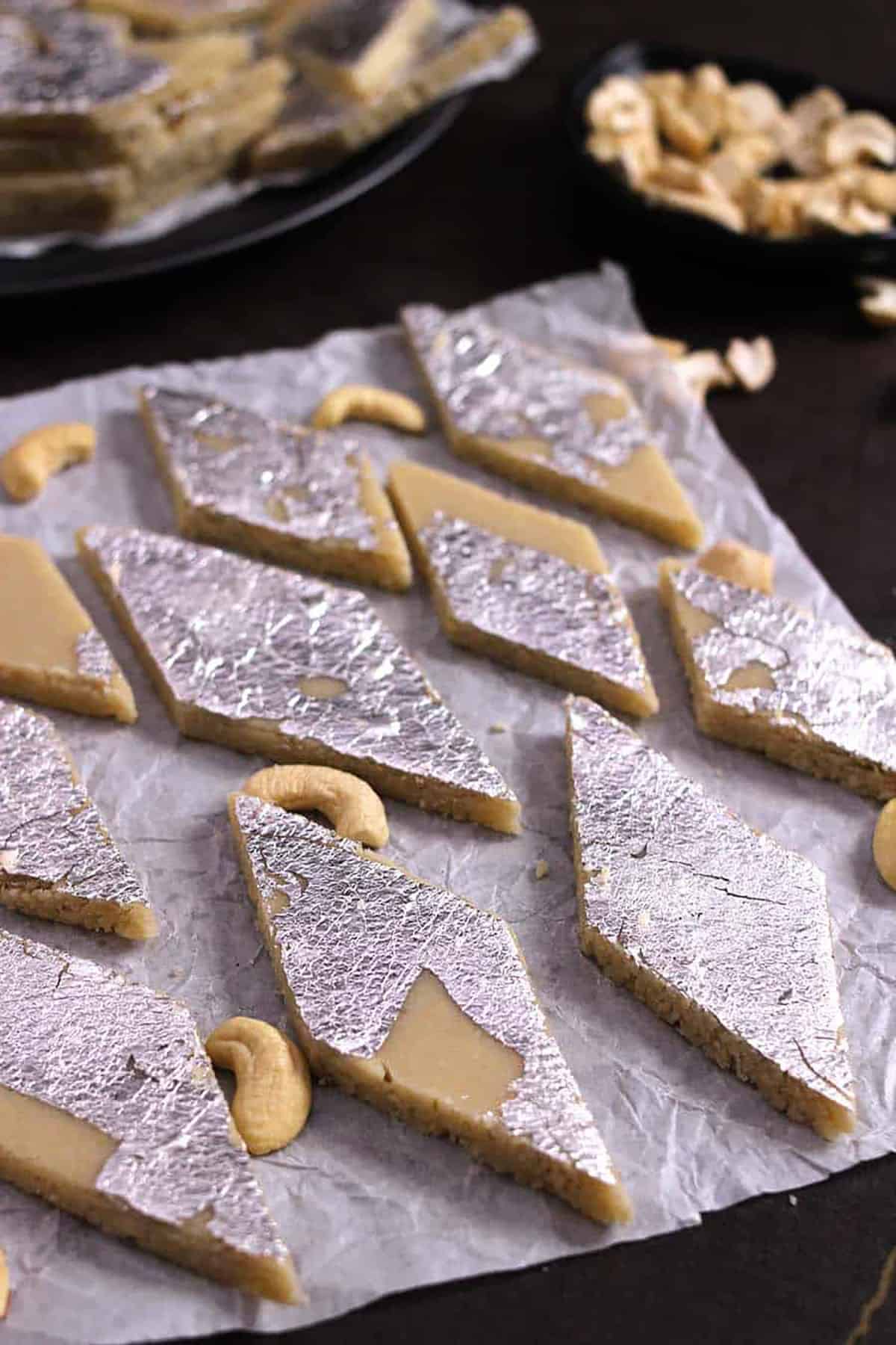 Kaju katli or burfi sweet slices with silver vark placed on parchment paper. 