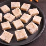 Best traditional Indian Coconut burfi (nariyal barfi) sweet bites on a black plate.