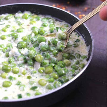 A spoon lifting creamed peas out of black skillet.