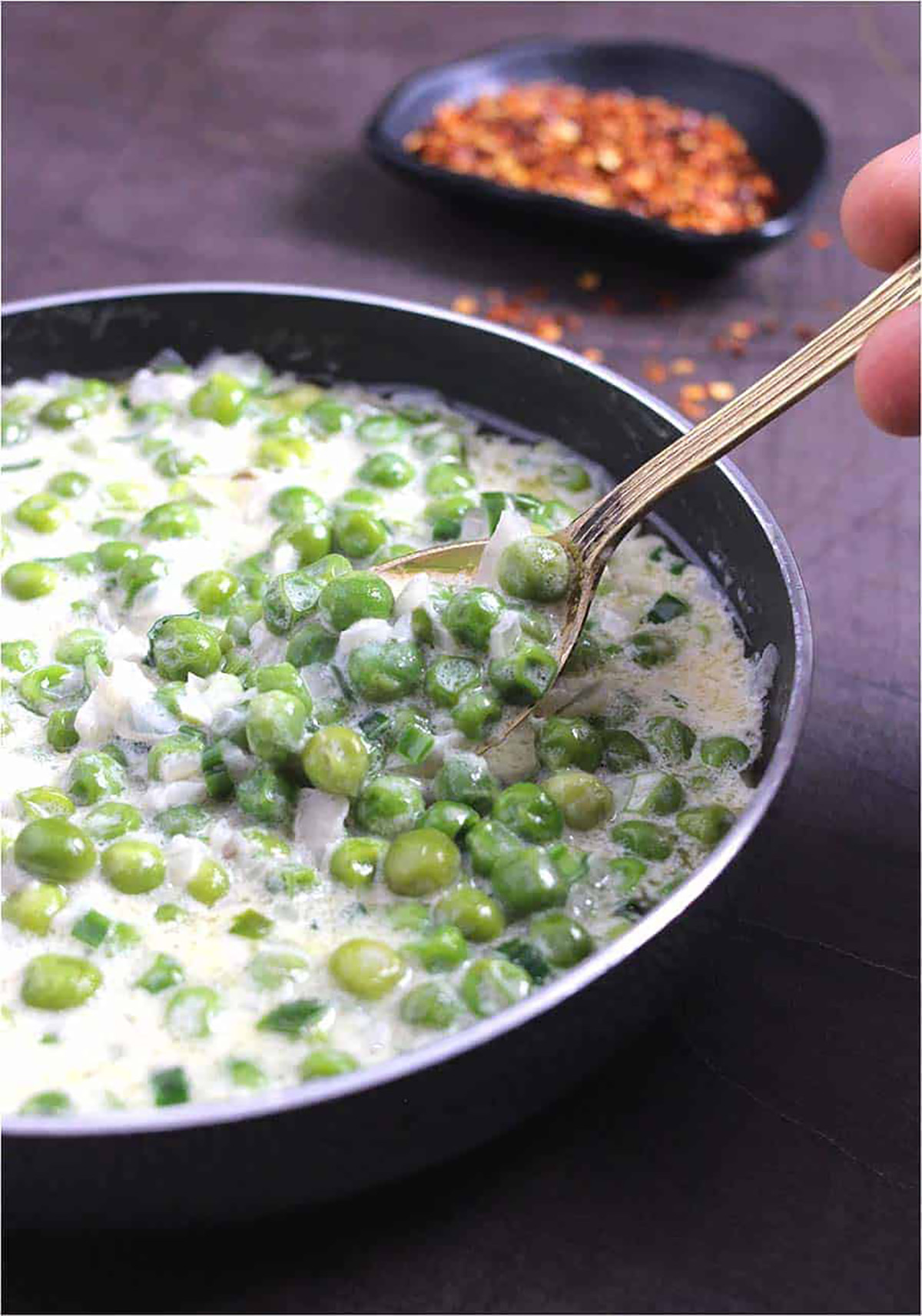 A spoon lifting creamed peas out of black skillet. 