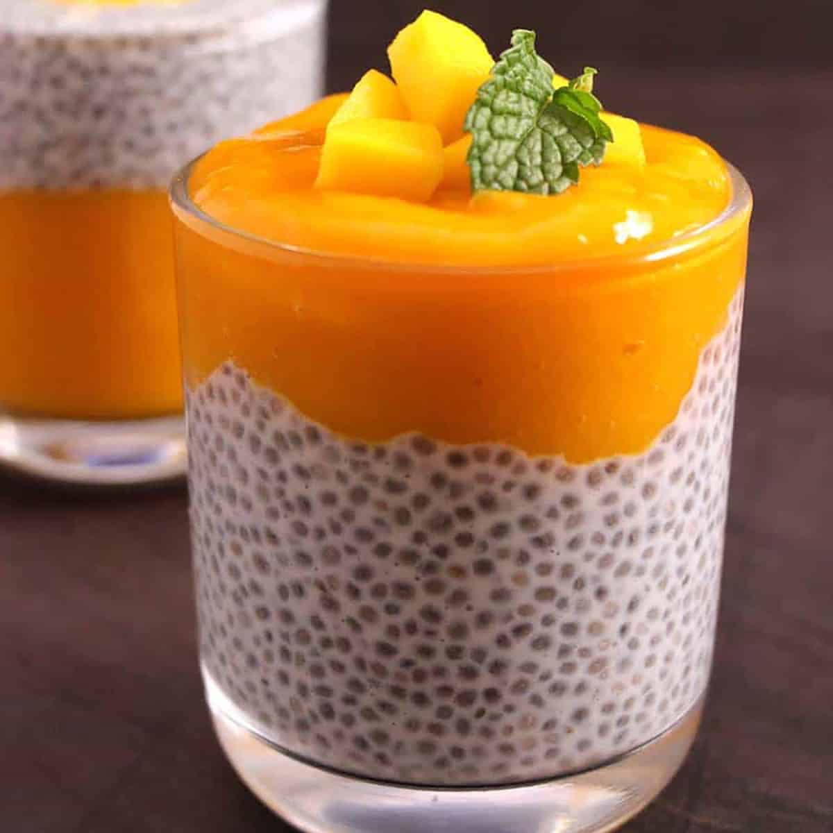 Overnight mango chia pudding in a serving glass garnished with mango chunks & mint leaves
