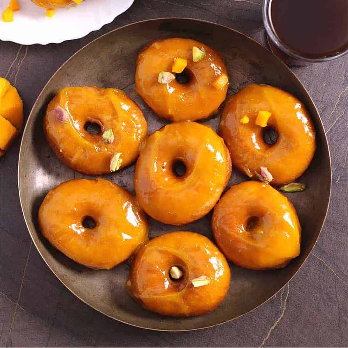 Mango doughnuts with mango glaze and cup of black coffee in the background. 