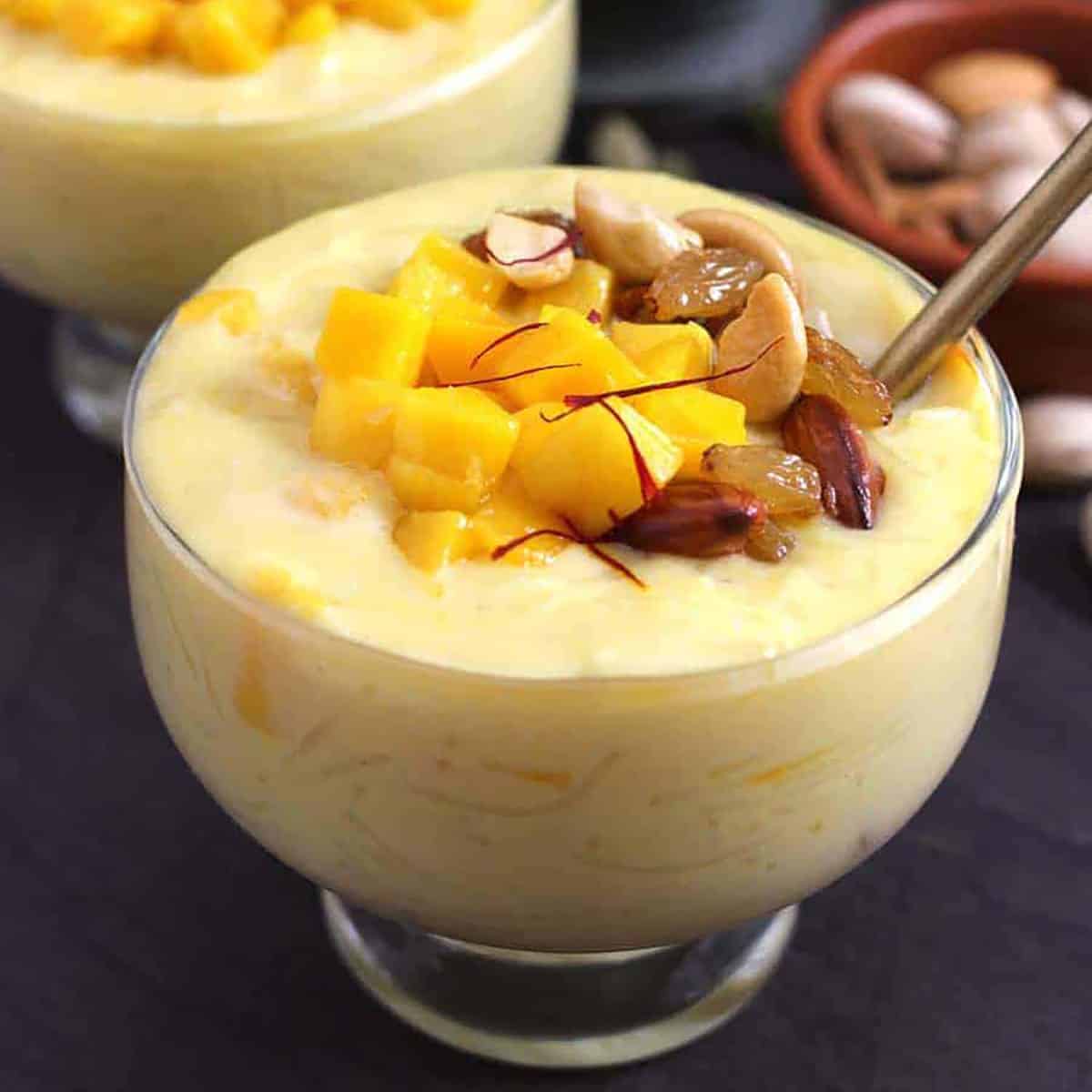 Mango vermicelli kheer served in bowl, garnished with mango, saffron, toasted raisins and nuts.