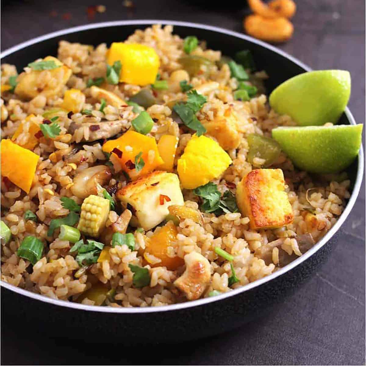 Thai mango fried rice with fresh mangoes, garnished with cilantro and served with lemon wedges.