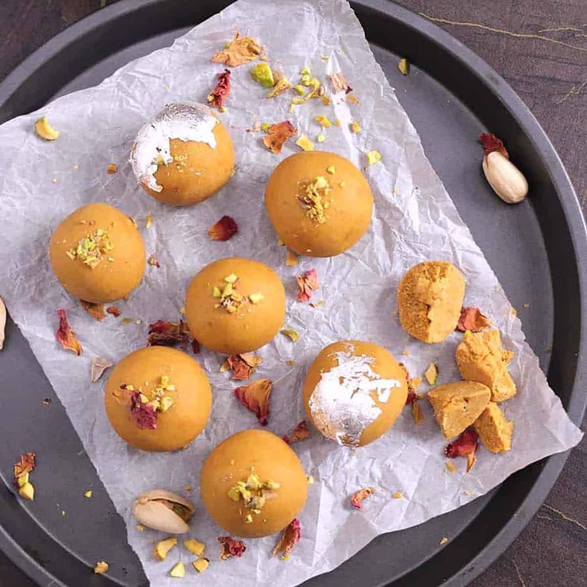 Top view of besan laddu garnished with crushed pistachios, dried rose petals, and silver vark.