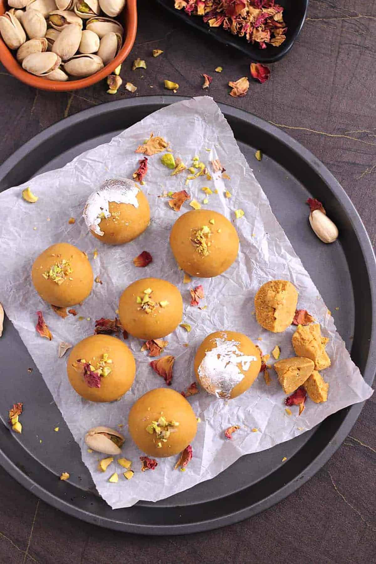 Top view of Besan Ladoo garnished with rose petals, crushed pistachios., and edible silver leaves or varq.