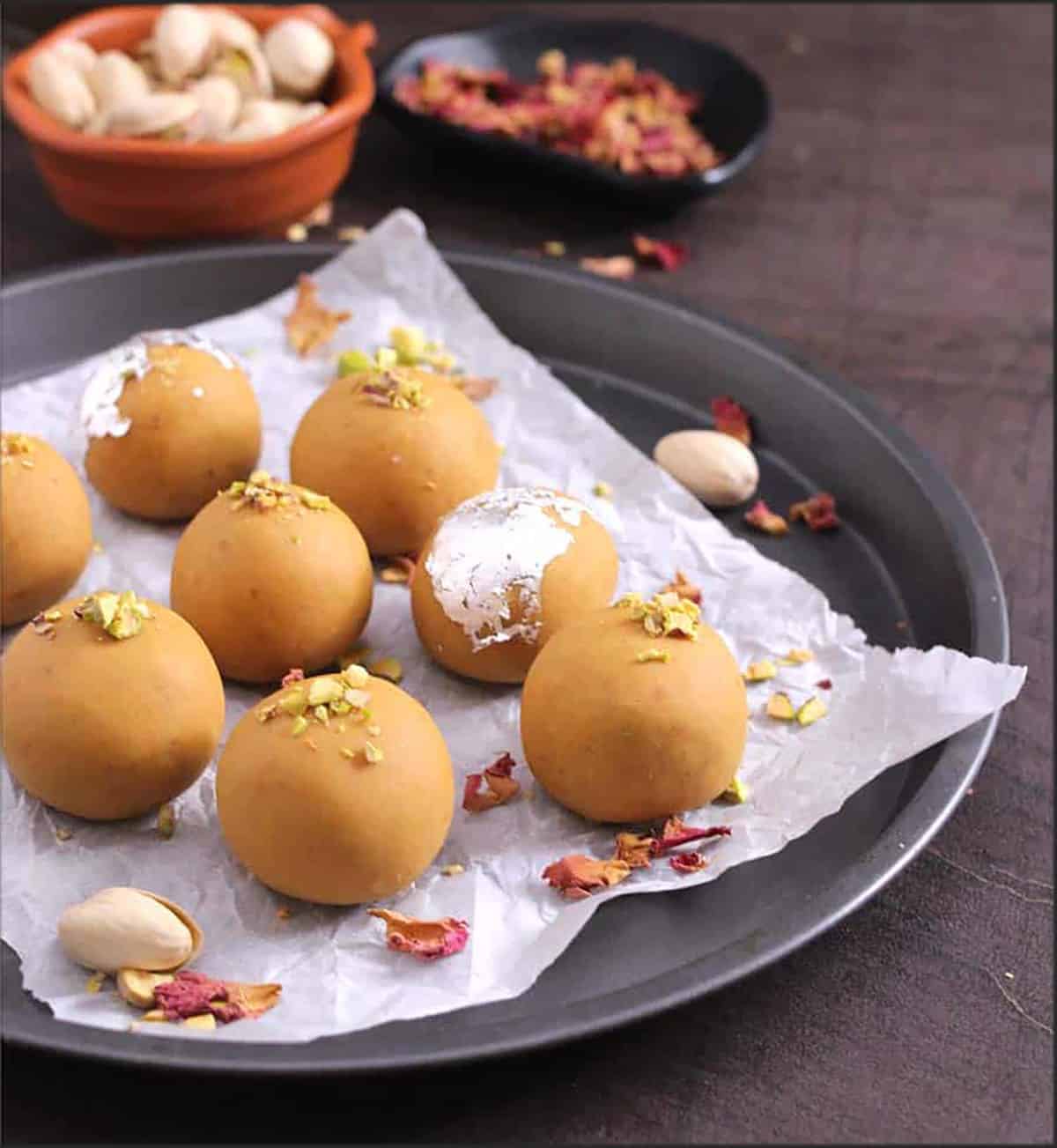 Besan Ladoo garnished with rose petals, silver vark. and crushed pistachios.