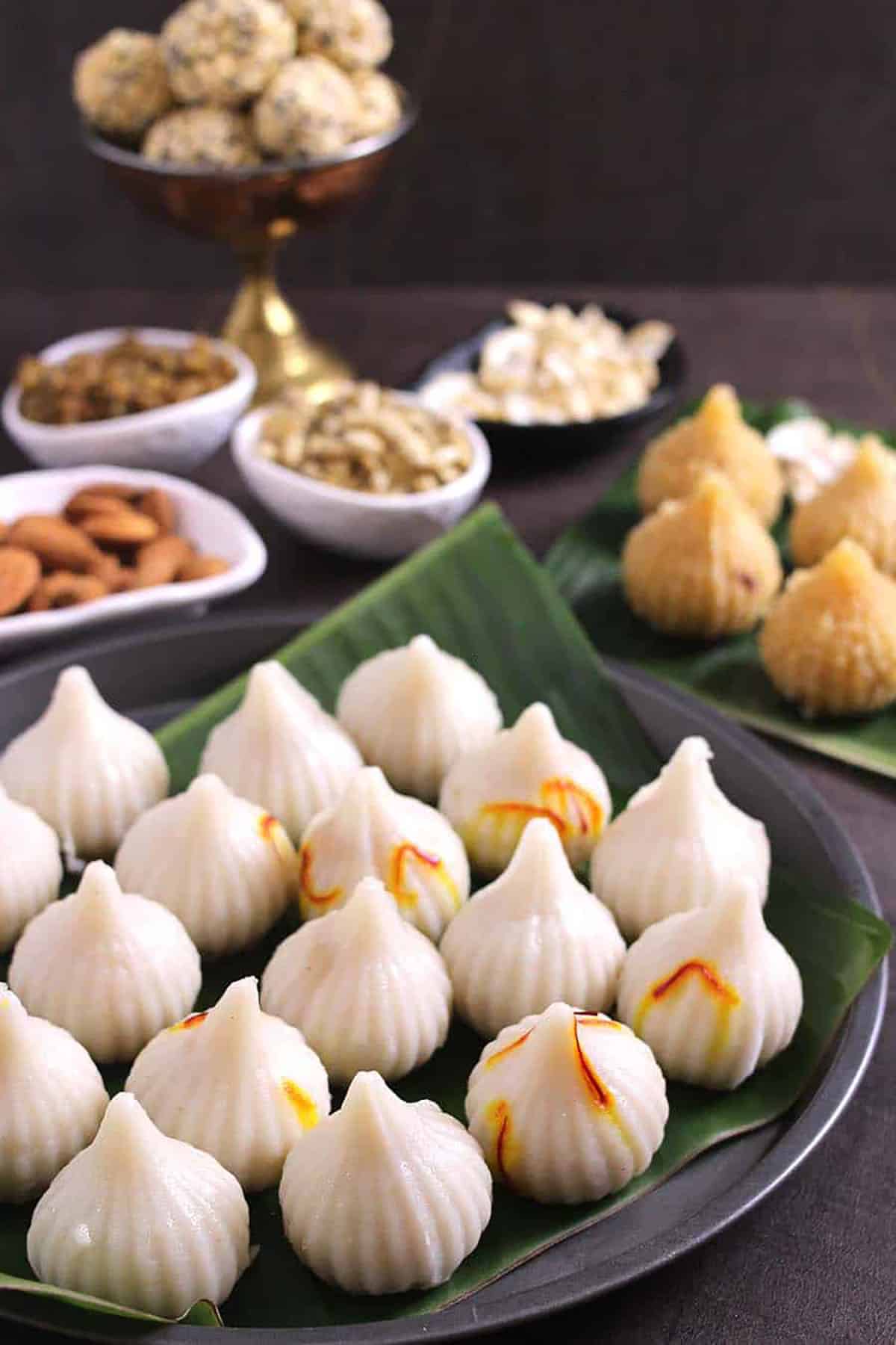 A tall shot of  steamed ukadiche modak, with a spread of other delicacies in the background.