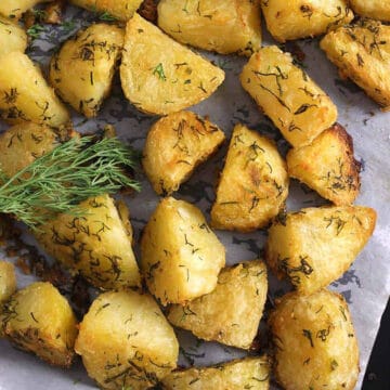 Close up shot of roasted garlic-herb potatoes garnished with fresh dill leaves and served in a baking pan.