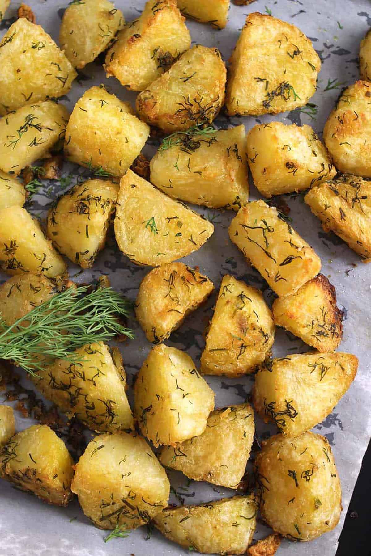 Top view of Roasted garlic-herb potatoes garnished with fresh dill leaves in a baking pan.