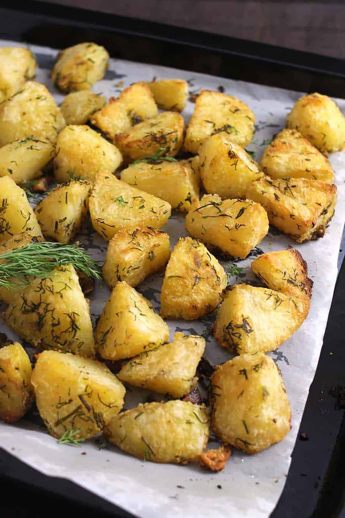 Zoom-out shot of Roasted garlic-herb potatoes garnished with fresh dill leaves in a baking pan.