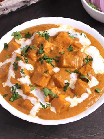 Paneer Butter Masala garnished with cilantro and a drizzle of cream and served in a white bowl.