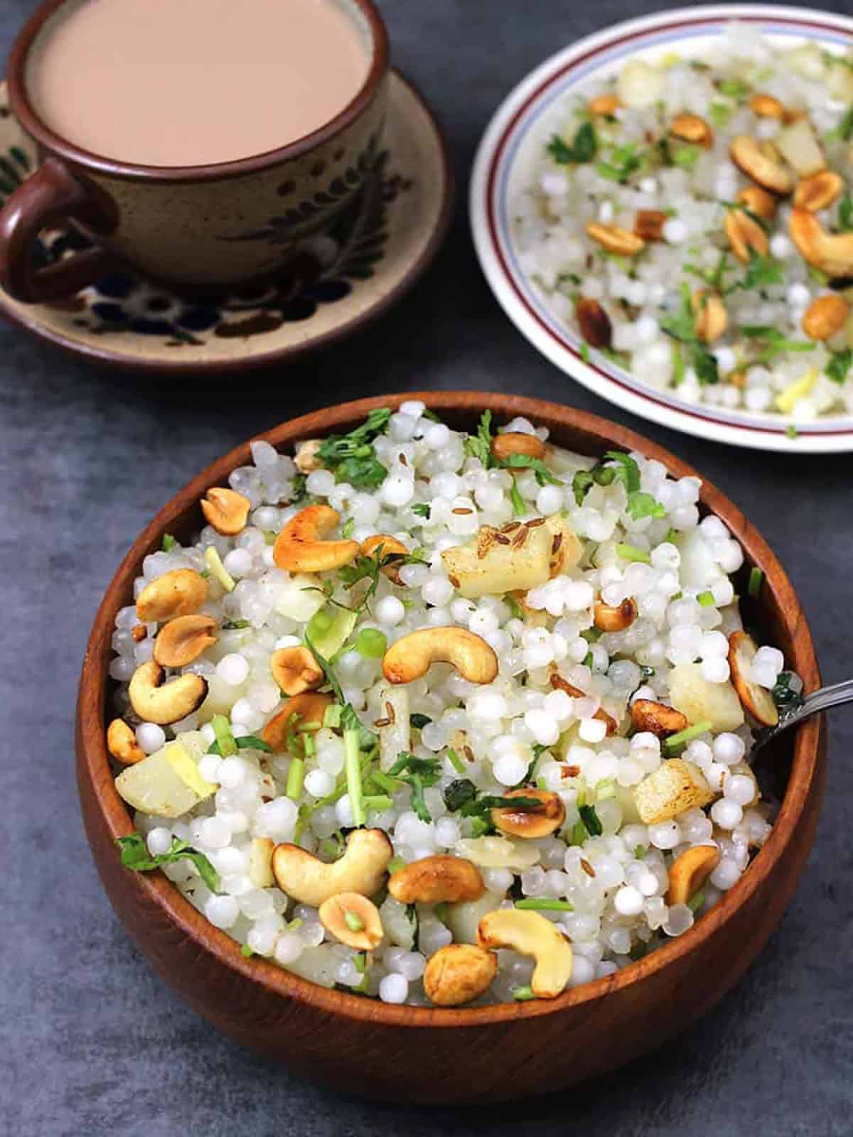 sabudana khichdi in a bowl garnished with roasted peanuts and cashews, served with a cup of hot chai.