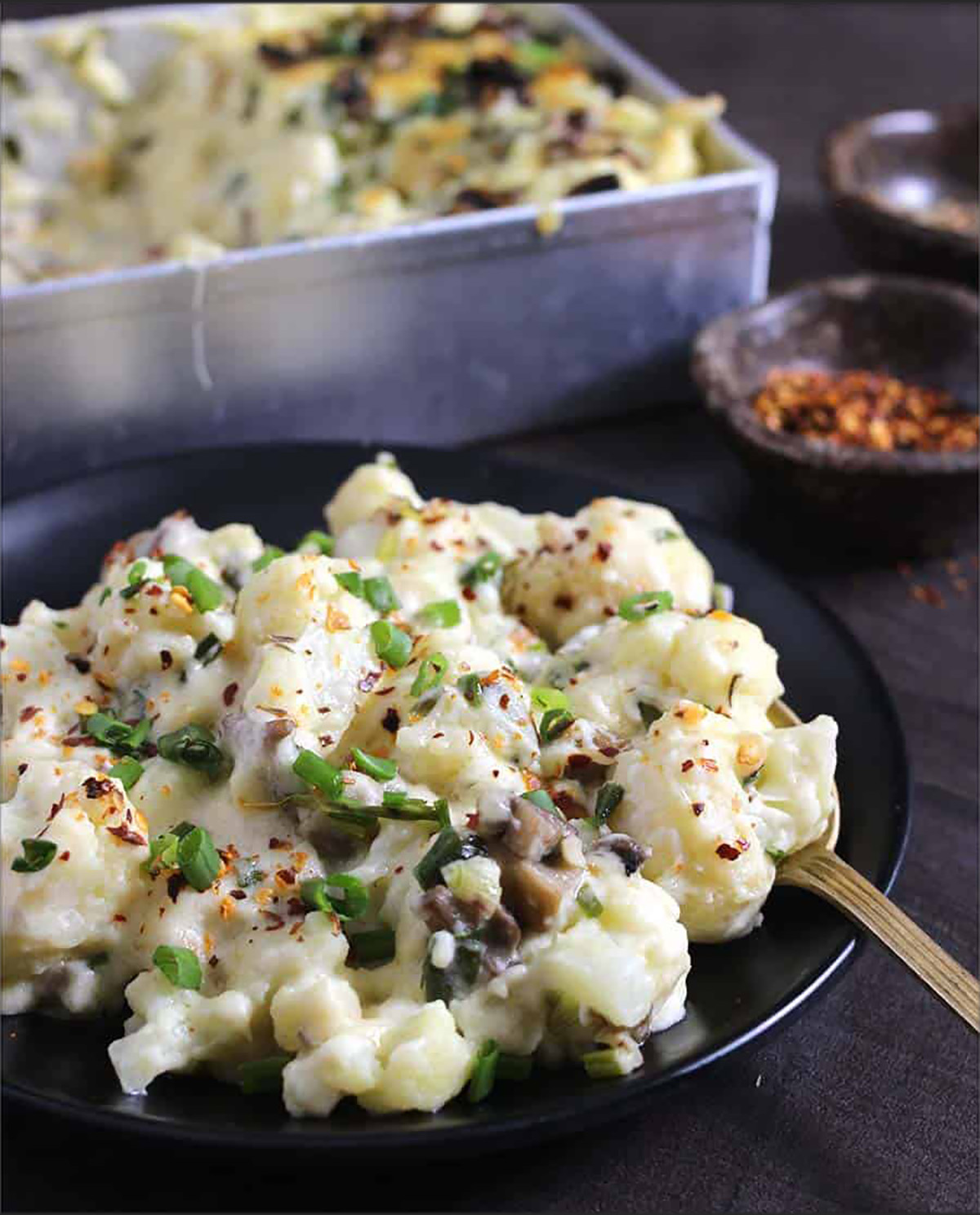 Cheesy cauliflower casserole bake with mushrooms served on a black plate for dinner. 