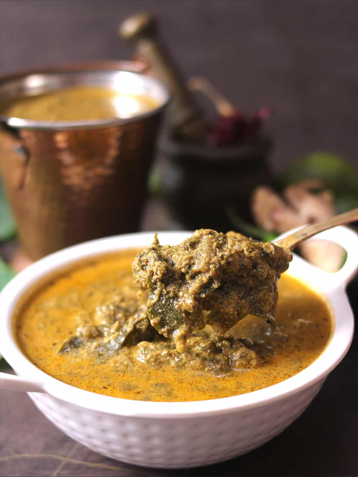 Alvati, konkani recipe prepared using taro leaves or colocasia leaves, holding curry in spoon 