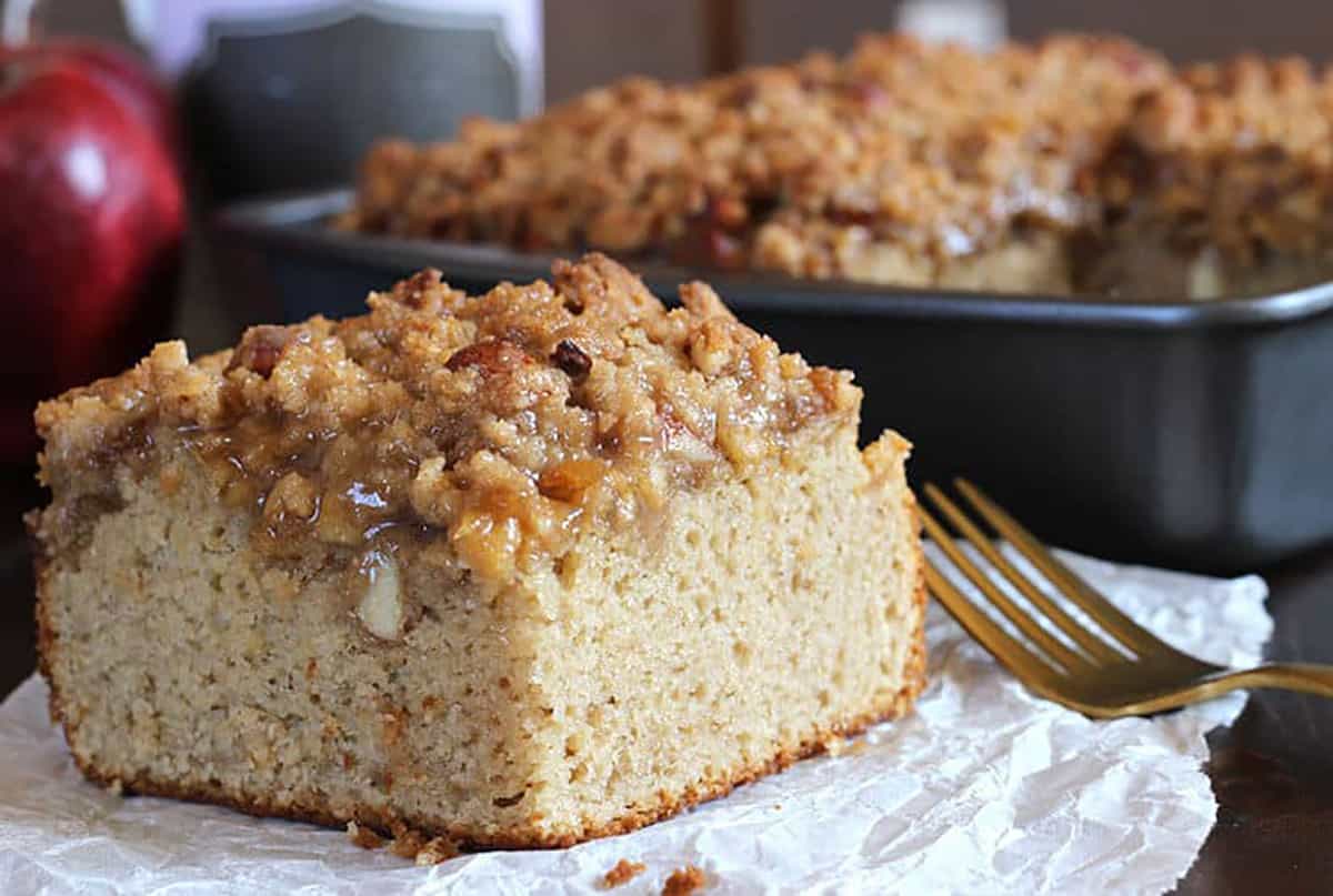 a slice of apple coffee cake with crumb topping served on parchment paper along with a golden fork.