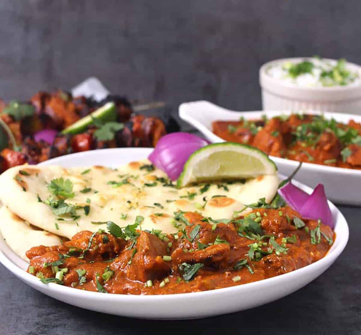 Authentic chicken tikka masala prepared at home that is serve in a white plate along with naan bread, red onion slices and a lemon wedge.